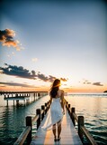 Fototapeta Pomosty - Kobieta w białej sukience stoi na molo i podziwia zachód słońca