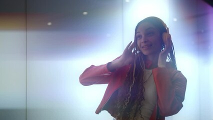 Alternative young woman with futuristic look and fashionable clothes in a bright led screens illuminated tunnel