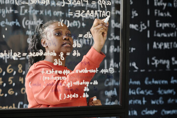 African American teacher writing codes on blackboard, she teaching IT lesson at school