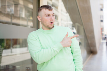 handsome man feeling joyful and surprised, smiling with a shocked expression and pointing to the side