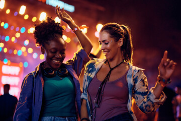 Wall Mural - Happy female festival goers dancing in front of music stage at night.