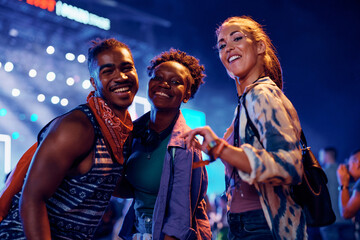 Wall Mural - Group of happy festival goers in front of music stage at night looking at camera.