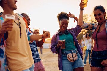 Wall Mural - Young carefree friends dance and drink beer during open air music concert.