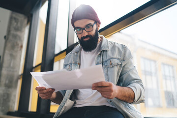 Smiling man reading documents near window in daylight