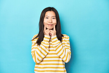 Asian woman in striped yellow sweater, doubting between two options.