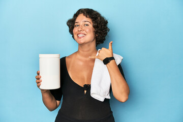 Young sportswoman with protein shake showing a mobile phone call gesture with fingers.