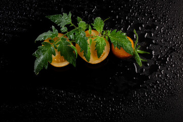 Wall Mural - Wet yellow tomatoes with flower and leaf on black background