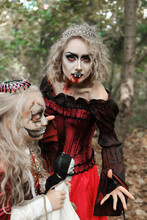 A Woman In The Form Of A Vampire Or A Sorceress And A Girl In The Form Of A Dead Princess With A Skeleton Doll In Their Hands Pose In The Forest. Image For Halloween. Mother And Daughter