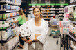 © Roman - Young woman looking to buy pack of toilet paper in supermarket.