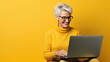 © Studio Nova - Elderly woman working on a laptop on a yellow background.