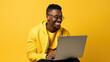 Young man working on a laptop on a yellow background.