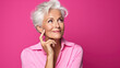 Senior thoughtful woman on pink background looking away.