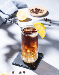 Wall Mural - Coffee cold brew with tonic in a tall glass with ice and lemon on a light blue background with coffee beans, fruits, napkin and shadow. Trendy summer craft refreshing drink