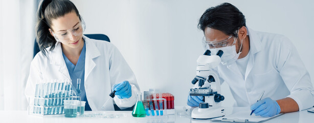 Professional scientist looking through a microscope in a laboratory with blood samples or tests, Science, analysis and medical technology concept.