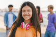 Portrait of smiling teenage girl in orange t shirt with headphones looking at camera on the street