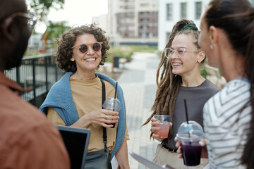 Aufkleber - Two young laughing Caucasian women with soda looking at their intercultural colleagues while chatting at break in urban environment
