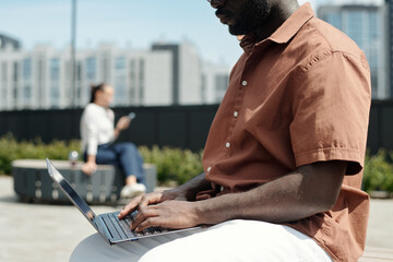 Fototapete - Cropped shot of young African American male analyst pressing keys of laptop keyboard while sitting in front of camera in urban environment