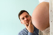 © Michael - Expectant father looks at naked baby belly of mother with uncertain look. Turquoise background. Bright shot.