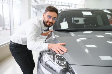 Happy young guy checking new luxury car, buying automobile at dealership centre. Portrait of cheerful millennial Caucasian man examining auto at showroom store