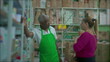 © Marco - A male black senior employee listening to female customer leaning on shelf and wearing green apron, supermarket grocery store small business setting