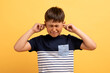 Angry unhappy irritated boy covering ears isolated over yellow background