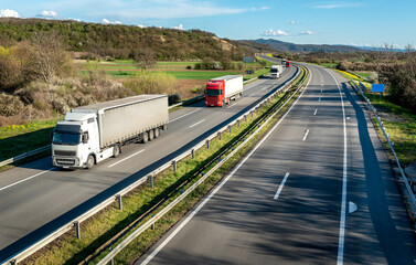 Wall Mural - Highway transport. Transportation Trucks in lines passing on a rural countryside highway under a beautiful blue sky