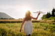 Back view of teen girl playing in dress with violet toy airplane during amazing sunset or sunrise. Childhood dreams. Family, nature, freedom and airplane concept. Playful cute child pilot