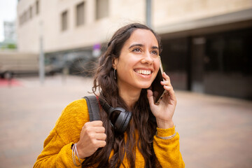 smiling young woman walking in city with bag and talking on phone