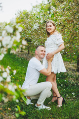 Wall Mural - Beautiful young couple in spring garden. Beauty lifestyle family concept. A happy mother is expecting a baby. A happy young couple in a blooming garden