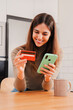 © Jose Calsina - Vertical portrait. Woman using a credit card and a cellphone doing a online shopping transaction, checking bank account at home. Female ordering a delivery by smart phone and paying the purchase. High
