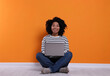 © New Africa - Happy young woman with laptop sitting near orange wall