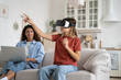© DimaBerlin - Mother freelancer working remotely on laptop while her daughter using vr glasses, sitting together on couch in living room. Girl playing with with virtual reality headset. Future technologies and kids