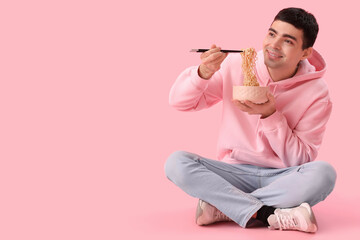 Young man with bowl of Chinese noodles sitting on pink background