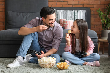 Poster - Father with his little daughter eating snacks while playing video game at home