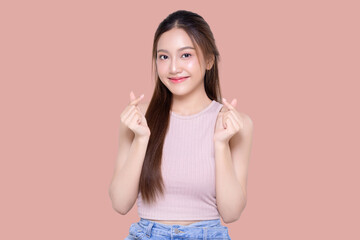 Beautiful young Asian woman shows mini heart fingers on isolated pink background. Facial and skin care concept for commercial advertising.