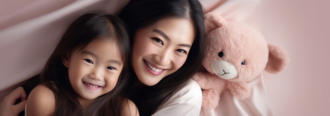 Wall Mural - Portrait of a Asian girl and mother on pink rose gold beige with bear doll background. World Mother's Day concept