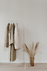 Wall Mural - Aesthetic minimalist neutral pastel beige colour wardrobe interior with dried pampas grass. Warm autumn outerwear on hanger over white wall. Fashion clothes