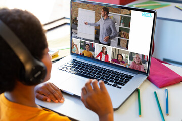 Wall Mural - Biracial boy having a video conference with caucasian male teacher and diverse students on laptop