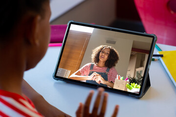 Canvas Print - Rear view of a african american boy having a video call with female teacher on a tablet at home