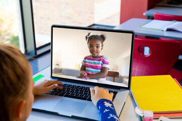 Wall Mural - Caucasian girl using laptop while having a video call with african american girl at school