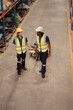 © Wosunan - Top view of two warehouse workers pushing a pallet truck in a shipping and distribution warehouse.