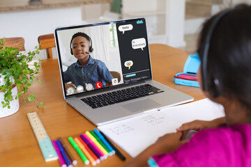 Canvas Print - Rear view of biracial girl having a video call with african american boy on laptop at home