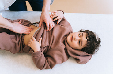 Top view on little caucasian boy laying on examining table at medical office, doctor touching boys stomach. Cropped image of nurse examining little kid after claims on pain at belly area.