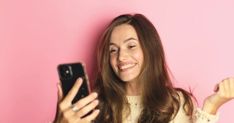 Happy young woman girl say wow hold in hand using mobile cell phone pointing fingers on workspace  isolated on pink background in studio. Happy winner girl, victory in lottery, good news.