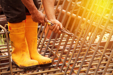 Worker securing steel rebar framing with wire pliers cutting tool at construction site. Yellow safety boots for construction