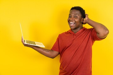 Photo of amazed Young latin man wearing red t-shirt over yellow background holding modern gadget arm head