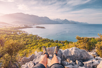 Hiker legs with trekking shoes on top of the canyon cliff with view of Kemer sea coast. Outdoors activity and skyrunning concept