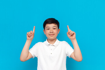 little asian boy in white t-shirt shows his hands up on blue background, korean child advertises copy space