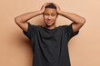 © wayhome.studio  - Photo of puzzled African man with short curly hair keeps hands on head feels overwhelmed dressed in casual black t shirt cannot decide his problems isolated over brown wall. Human reactions concept