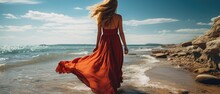 Woman In A Flowing Long Red Dress Walks On The Beach, A Photo Taken From Behind Her. Generative AI.